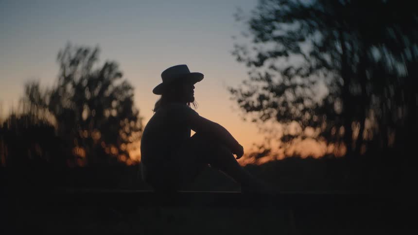 Silhouette of a person sitting on a hill in the wilderness enjoying the sunset