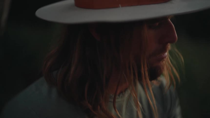Man wearing widebrimmed hat and green shirt is seen in profile looking downward