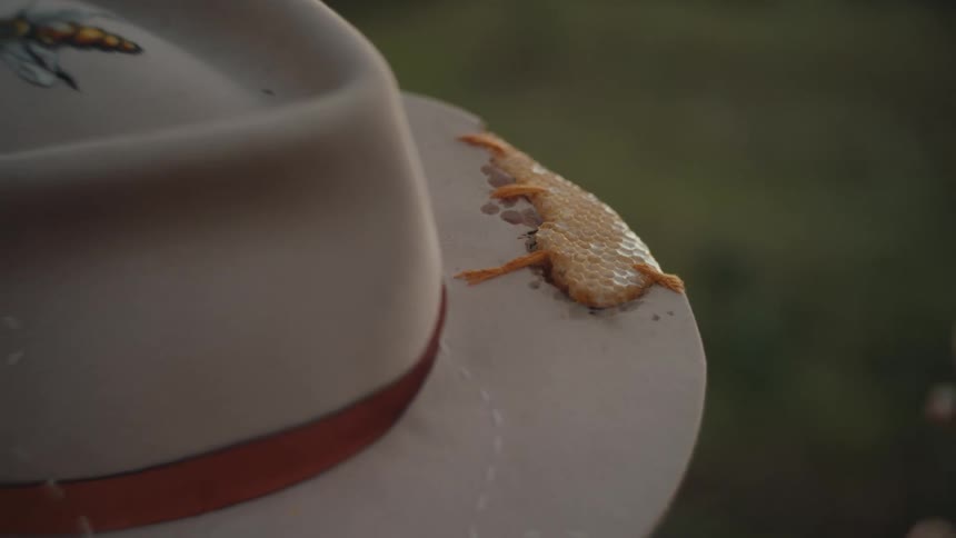 A person outdoors at midday wearing a brown cowboy hat adorned with artistic drawings on the crown