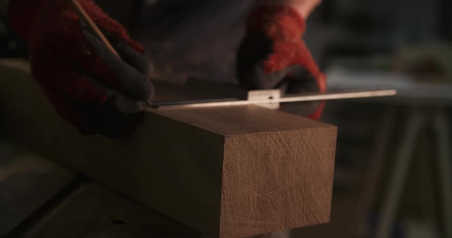 Gloved hands mark measurements on a wooden block with a metal ruler