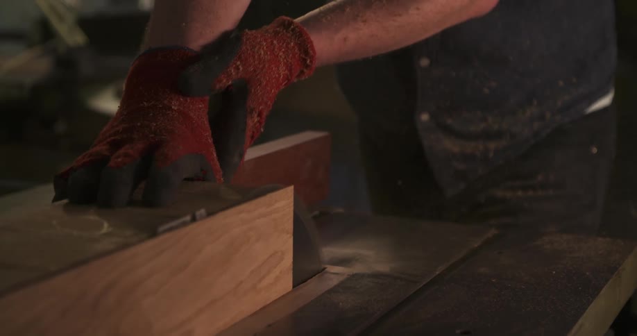 The video shows a closeup of a person wearing orange and black gloves operating a table sawthey are ripping a piece of hardwood lengthwise and at the end of the short clip they remove the cut piece from the table