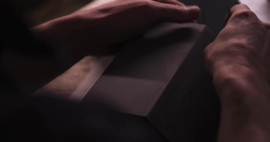 Hands carefully adjust a dark piece on the workbench
