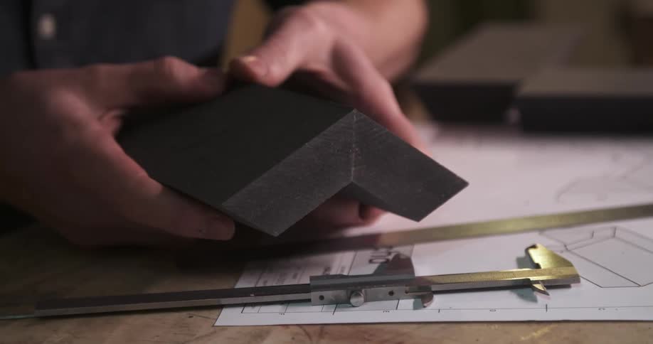 A craftsmans hands carefully align two precisely cut pieces of wood over blueprints with a caliper resting nearby on the workbench