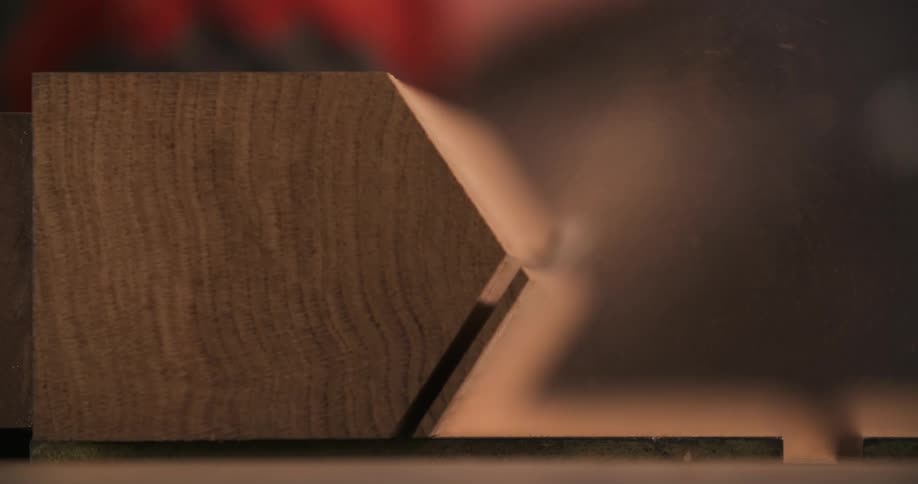 Gloved hands using a power tool to cut a piece of wood in workshop