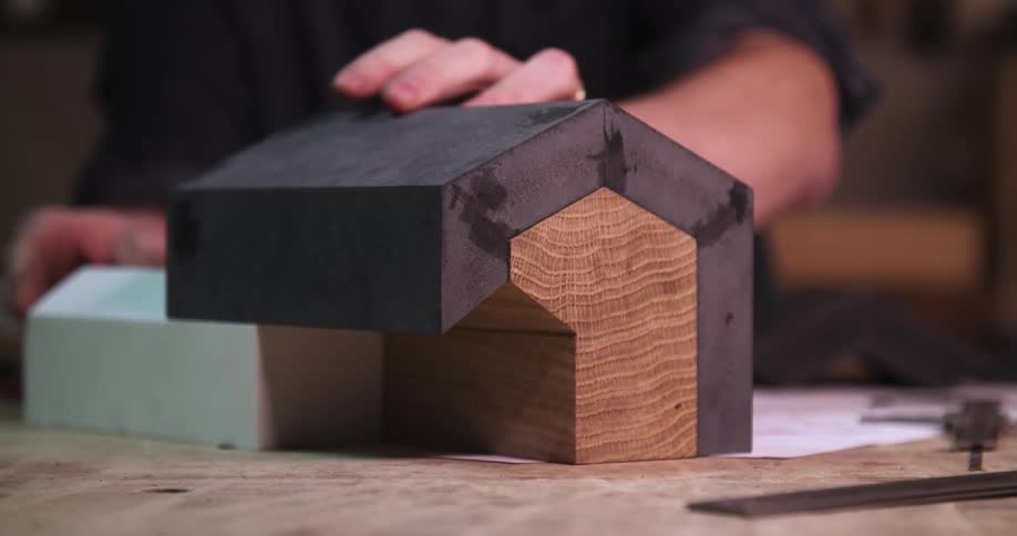 Close up of a male carpenter assembling a wooden structure on a desk in a workshop