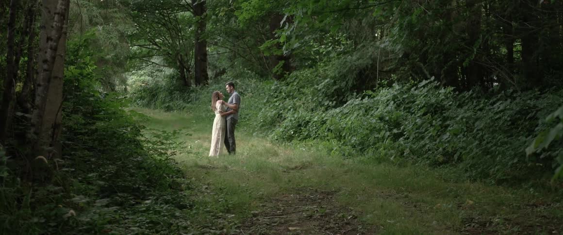 A couple standing on a path in the woods embraces