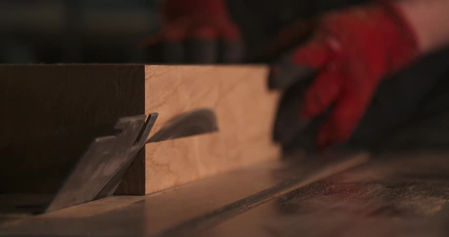 A carpenter cutting wood with an electric saw on a workbench inside a workshop at midday