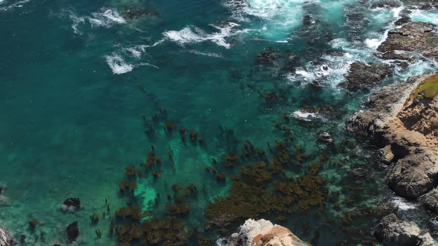An aerial view of waves crashing against a rocky coastline