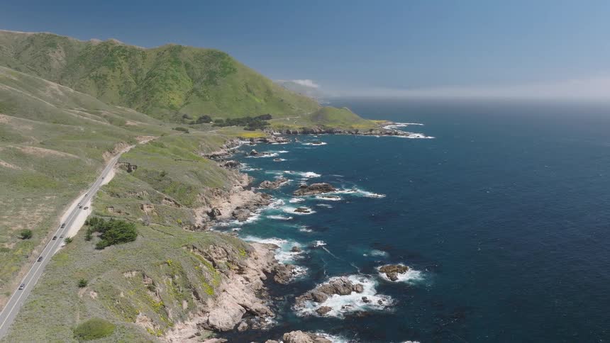 Rocky cliffs border the blue sea beside green hills