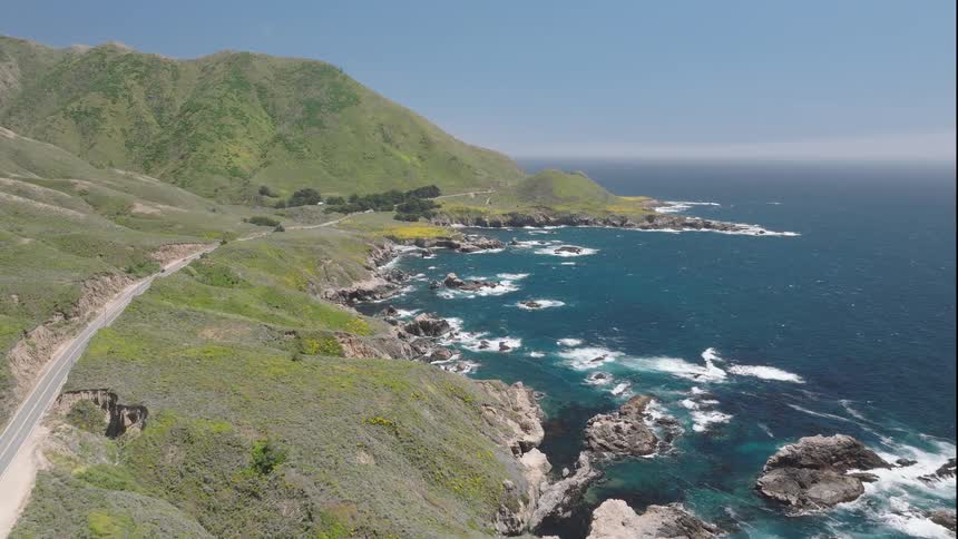 Coastal road winds beside green hills and deep blue sea
