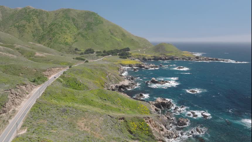 Winding coastal road beside green hills and blue sea