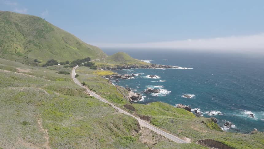 Coastal landscape with green hills and a road near the deep blue sea
