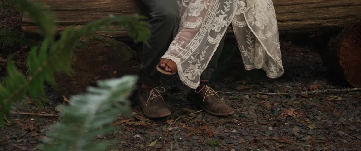A man and woman are sitting on a log with their legs intertwined