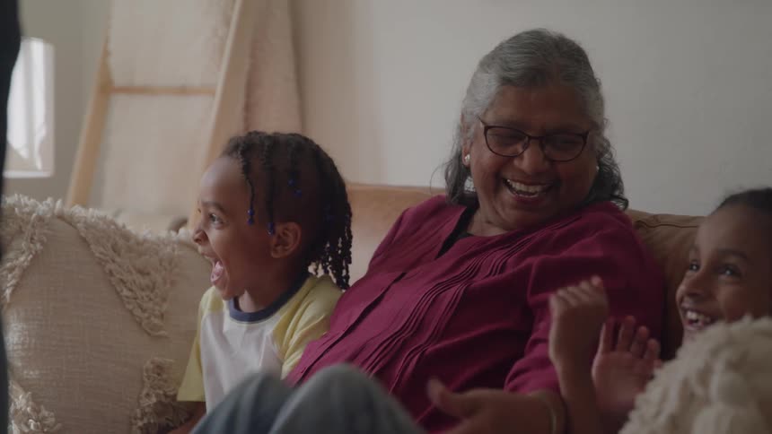Children and an older woman laugh together while sitting on the couch