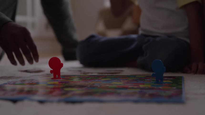 Two people play a board game on the floor with red and blue pieces