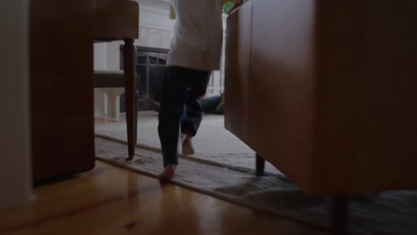 A young male child running to meet his mother sitting on the floor in the living room to play during daytime