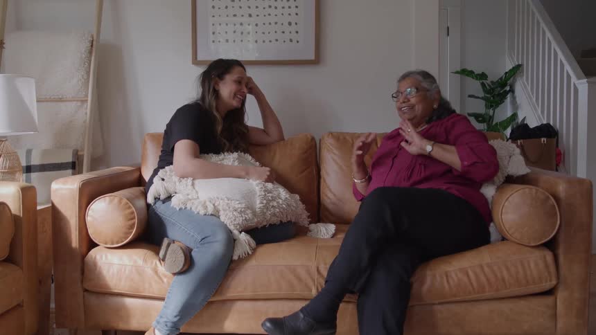 Two women chat and smile while sitting on a couch in the living room