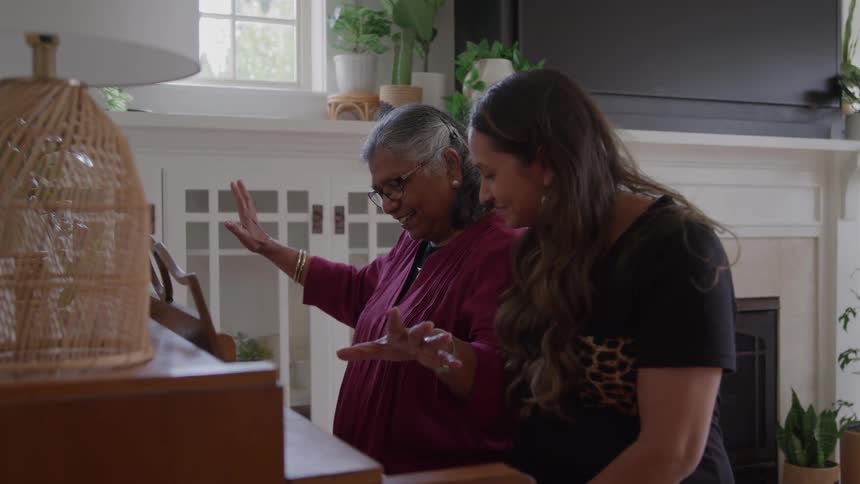 A young woman tutoring an elderly woman on piano step by step in a sunlit living room at midday both focused and smiling