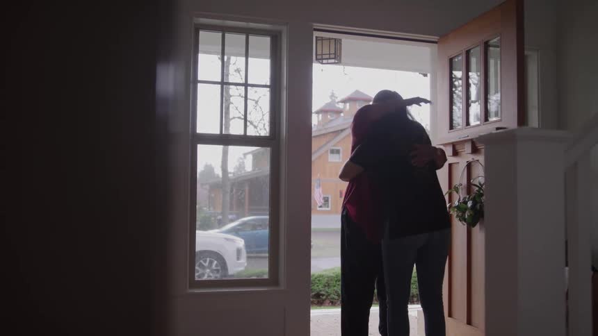 Two people share a warm hug at the front door of a house