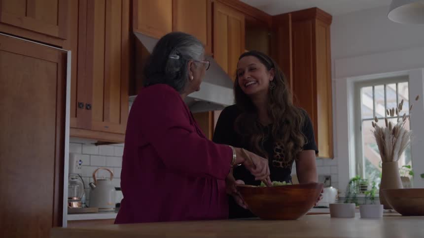 Two people prepare a meal together in kitchen with wooden cabinets and white tiled wall