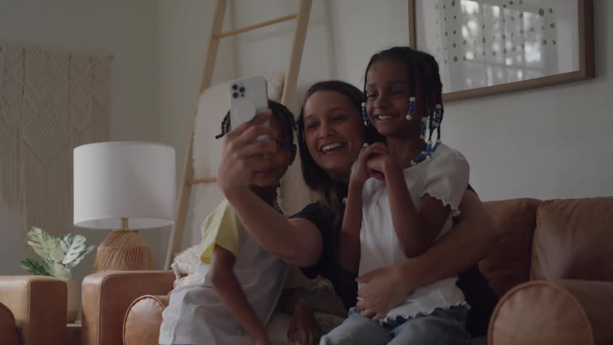 Woman and two children smile together while taking a selfie on the couch