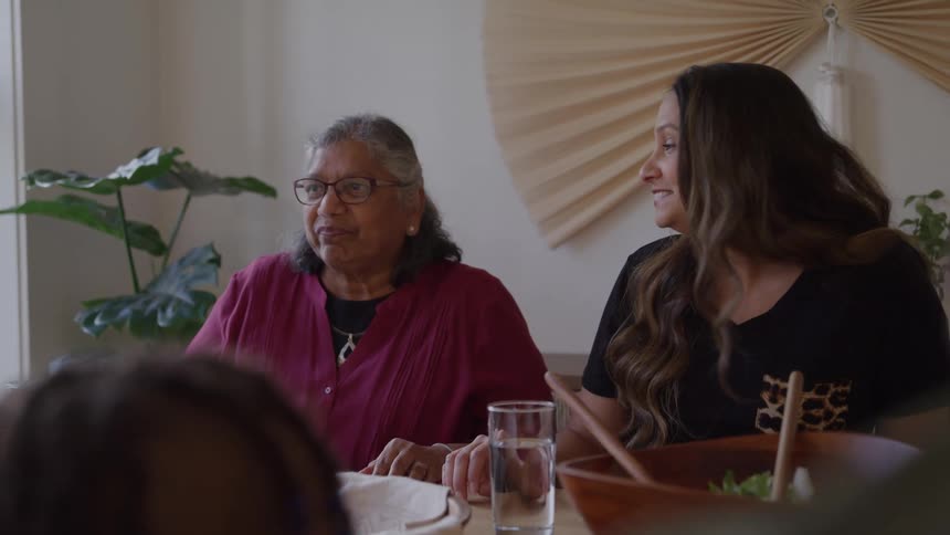 A group of women sitting around a dining table at midday engaged in a lively and fun discussion that prompts an elderly woman to burst into laughter