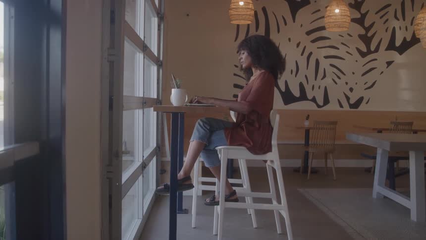 Woman works on a laptop while sitting alone in a bright caf