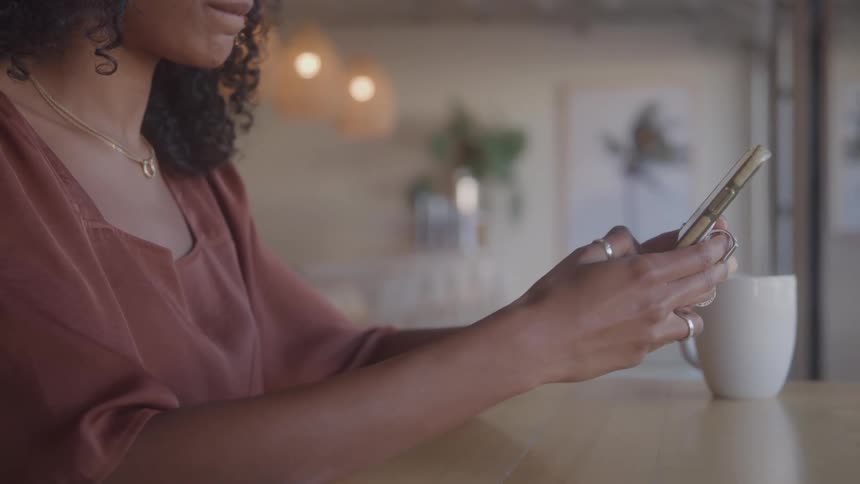 A young black woman sits and text on a smartphone in an indoor setting