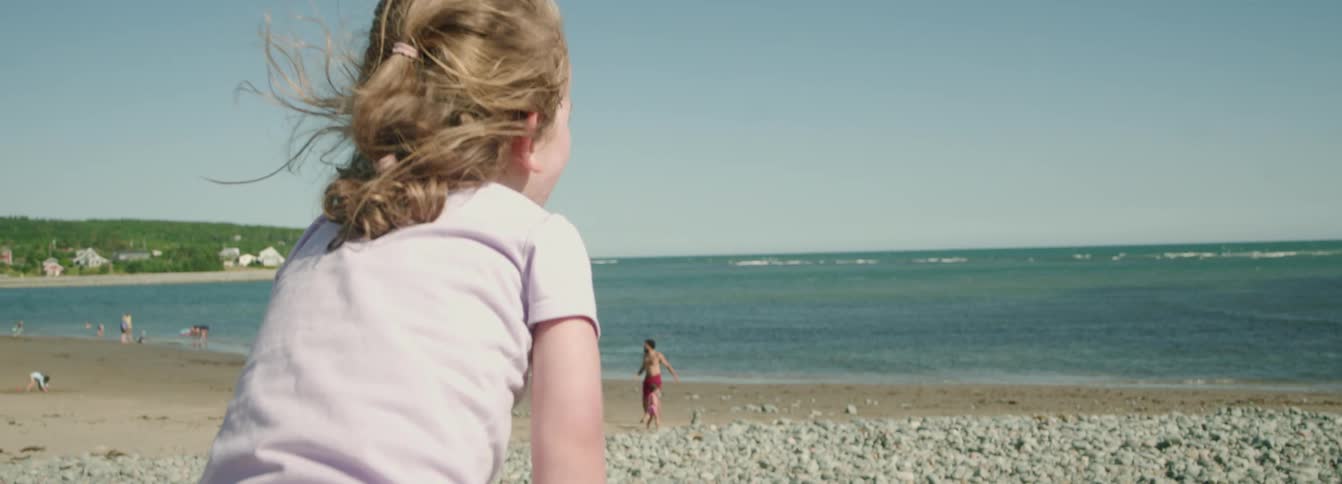 Child watches the sea as the wind blows her hair on the beach