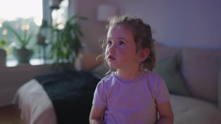 Child in a pink shirt watches something attentively in the bright living room
