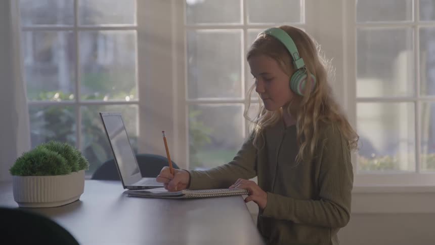 The girl is wearing headphones while writing in her notebook