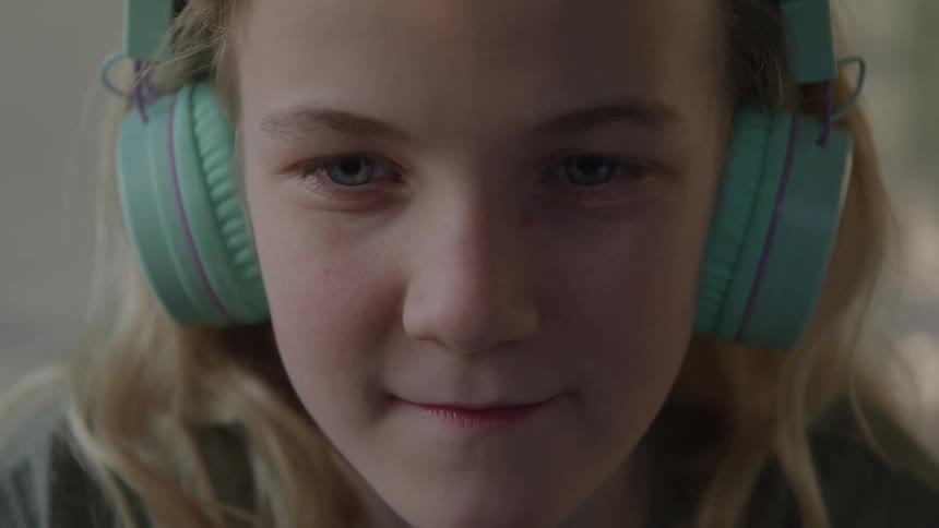 Child smiles subtly while listening to something with green headphones