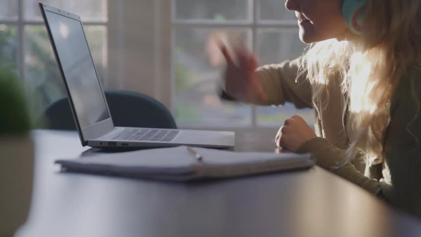 The girl smiles and waves at the laptop