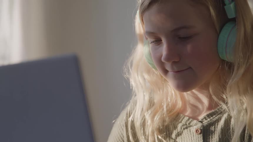 A child wears headphones and looks intently at a laptop screen