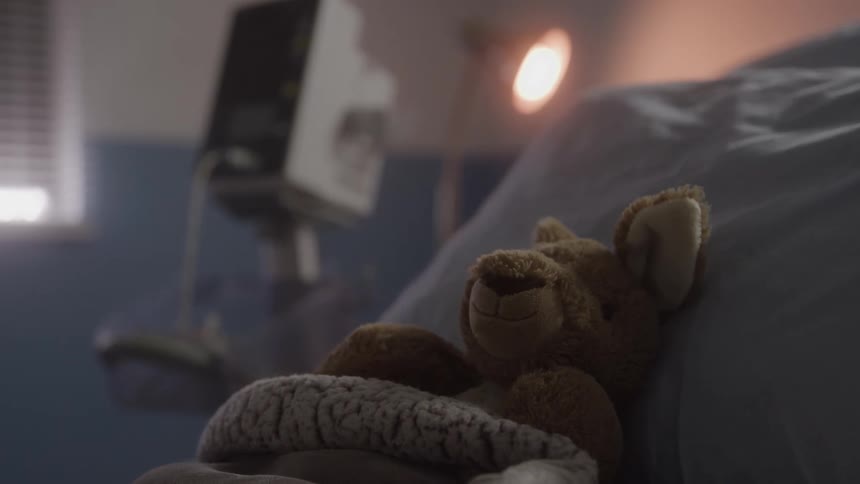 Stuffed bear covered with a blanket on a hospital bed