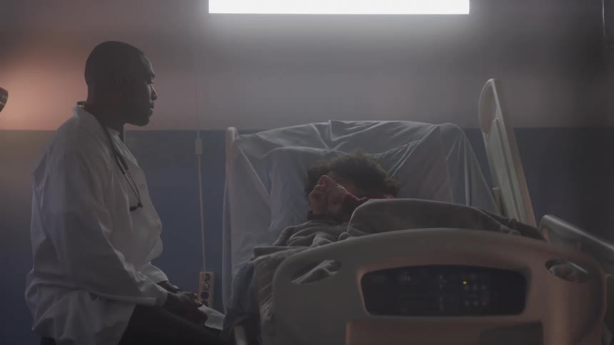 Doctor sitting beside a patient lying in a hospital bed