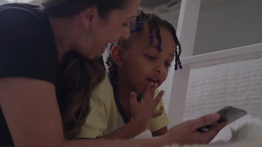 A person and a child lie down next to each other and look at a phone