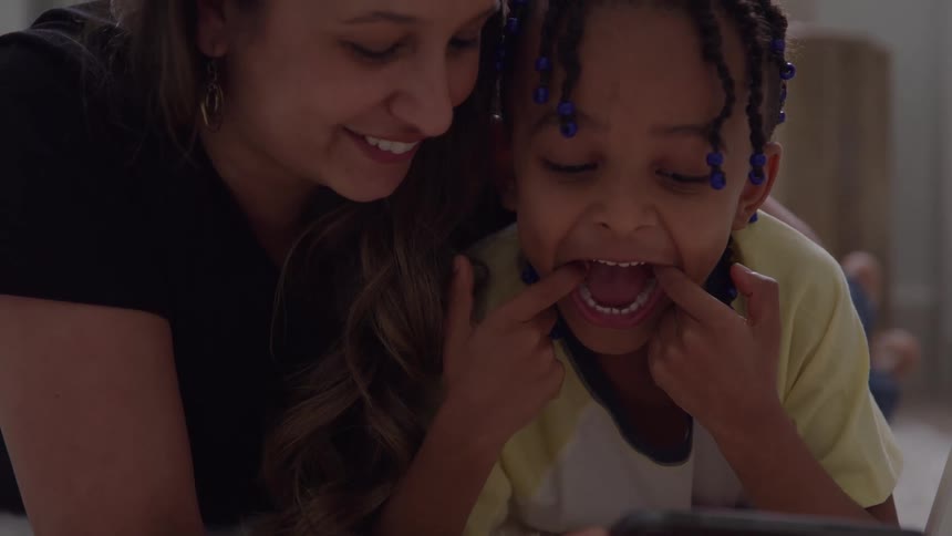 Child making a funny face while being watched by a smiling woman