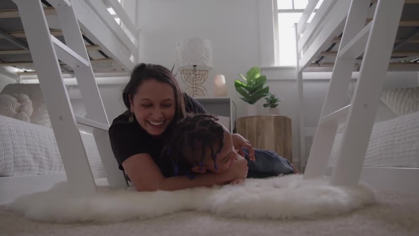 A mother and child playfully lie on a fluffy white rug between two bunk beds laughing and interacting affectionately