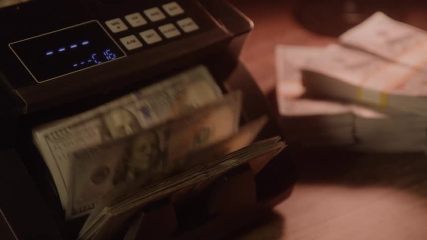 Counting machine in operation with dollar bills and stacks of money in the background