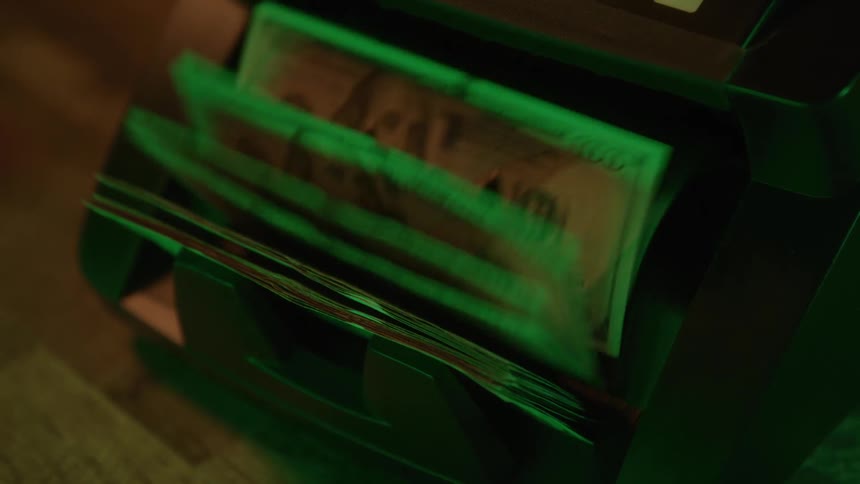 Dollar bills being rapidly counted in a machine under intense green light