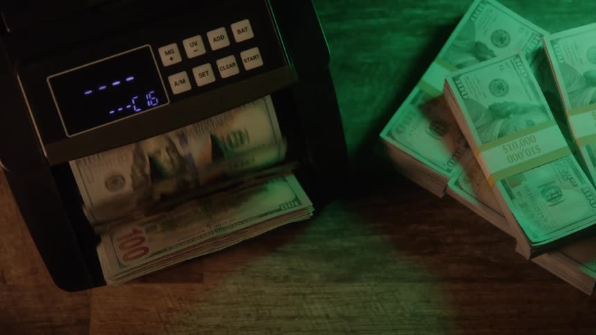 Automatic counter processes 100 bills beside neatly stacked bundles on wooden surface