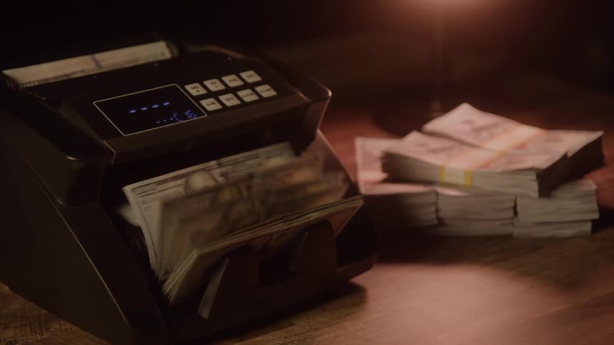 Counting machine operating next to stacks of dollar bills on the table