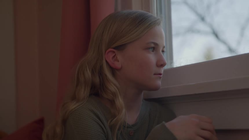 The girl is peering out the window