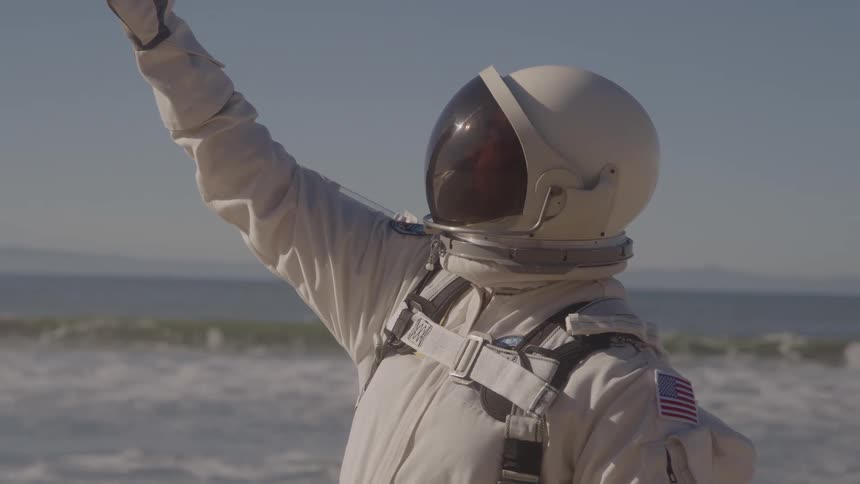 The astronaut raises their hand on the beach