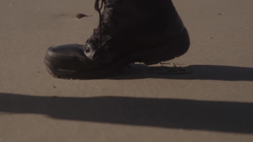 Black boot leaving a footprint on the wet sand