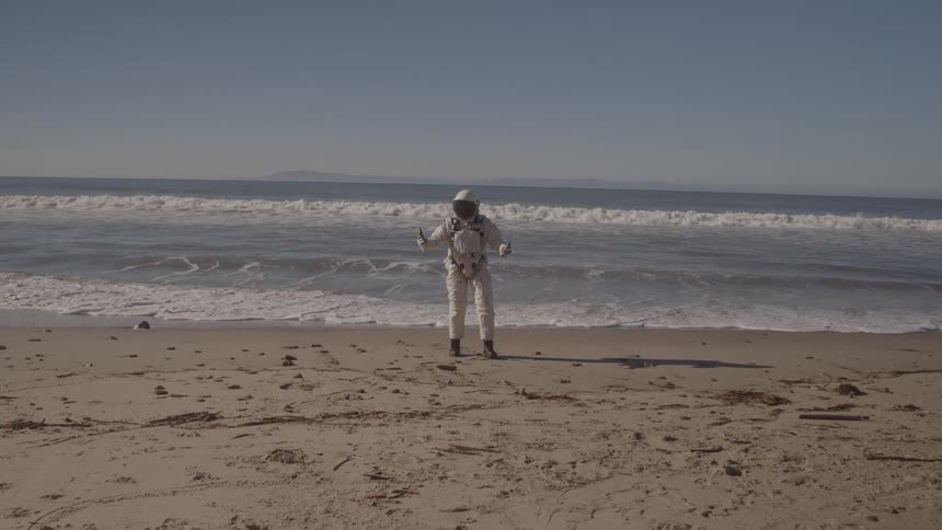 Person in a spacesuit walking alone on the sand toward the sea