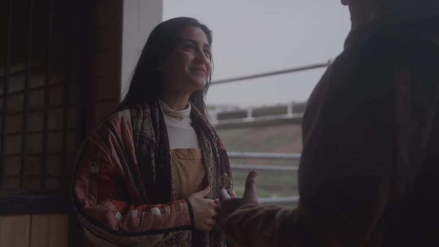 The woman is smiling and listening to a man in the stable