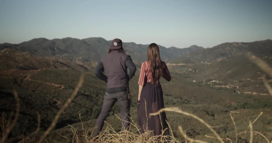 A man throws a stone as he and a woman stand overlooking a view