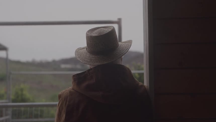 The man is leaning against the doorway of the stable